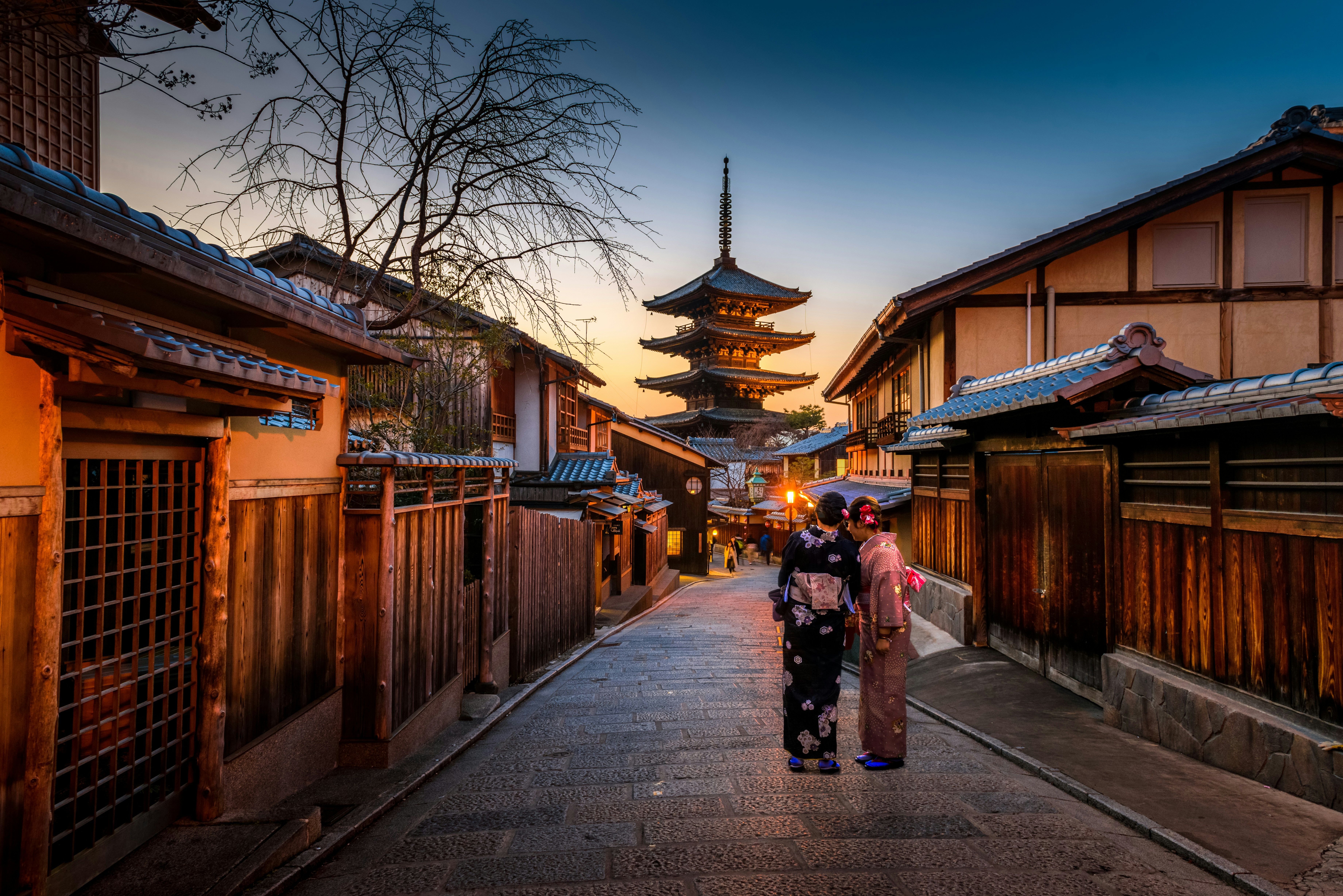Two women wearing traditional purple and pink kimonos standing on a street in Japan.